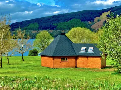 a small wooden house in a field with a lake at Seal Cove Cabin - Luxury Glamping in Cairndow