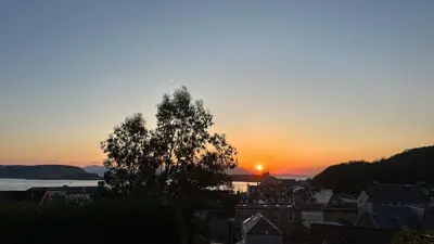 a sunset over a city with a tree in the foreground at Kenavara House in Oban